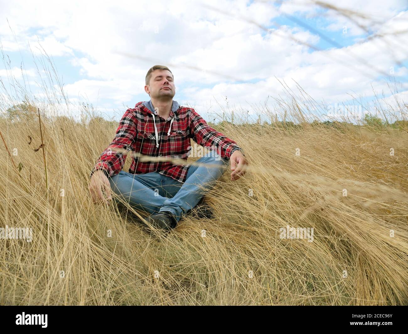Young tourist sits in the grass on the autumn field. Relaxation and Meditation. Stock Photo