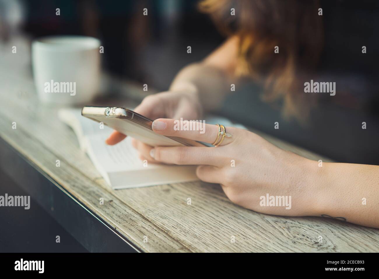Crop unrecognizable Woman sitting at window in cafe and using smartphone Stock Photo