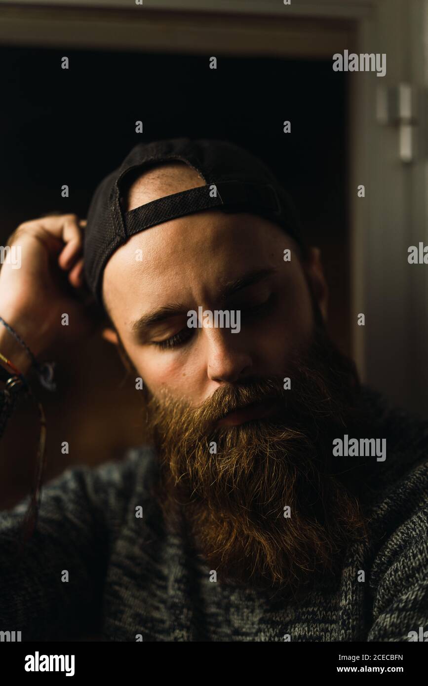 Portrait of young man with beard wearing cap and looking thoughtfully down. Stock Photo
