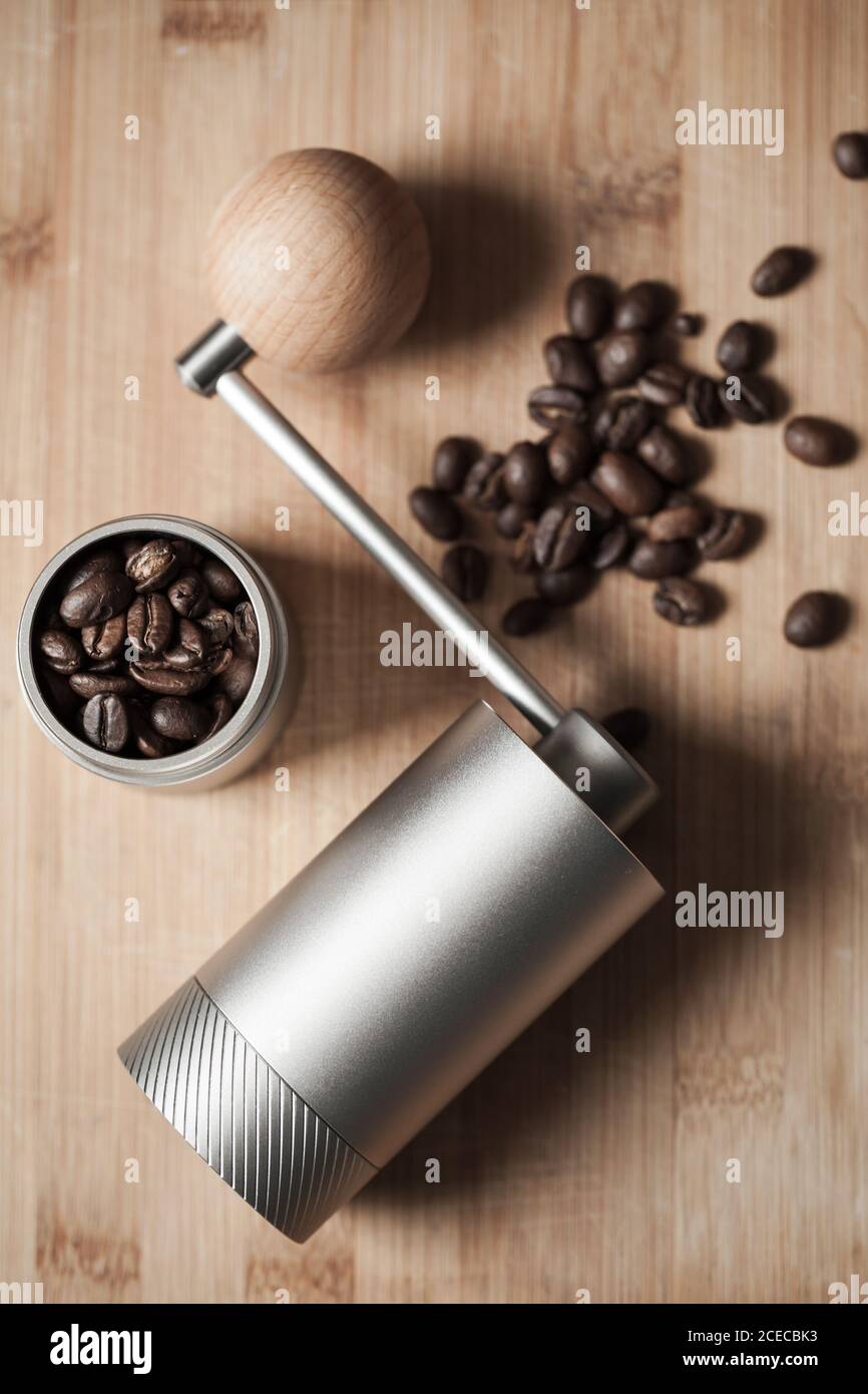 Shiny manual coffee grinder and roasted coffee beans are on wooden desk, vertical flat lay photo with soft focus Stock Photo