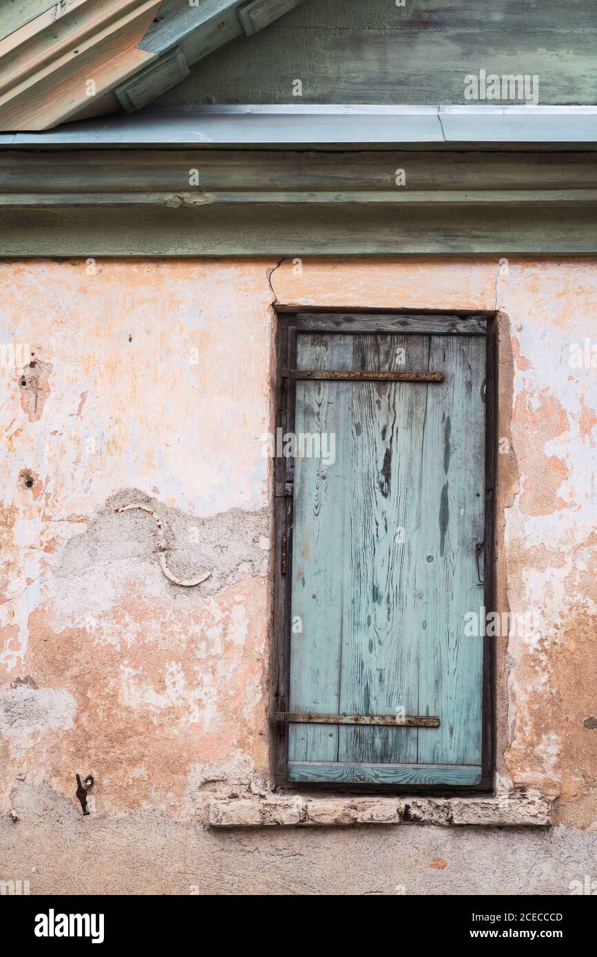 Narrow window with shabby timber shutter located on crumbling wall of old house Stock Photo