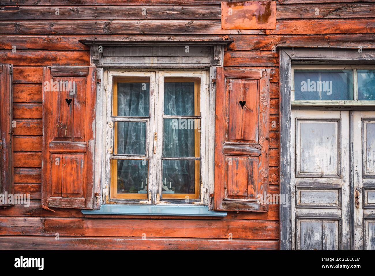 Small window with lovely shutters and shabby door of nice lumber house in small settlement Stock Photo