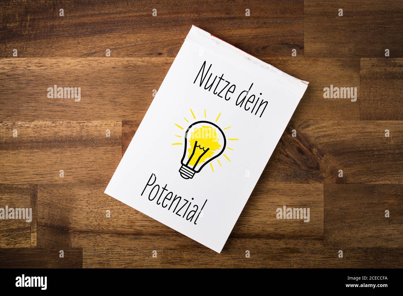 Nutze dein Potenzial - German Text - Translation: use your potential - light bulb and text on a notepad Stock Photo