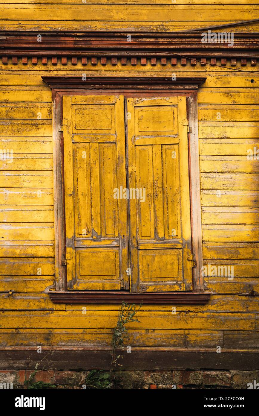 Window with closed shutters located on lumber wall of yellow countryside house Stock Photo