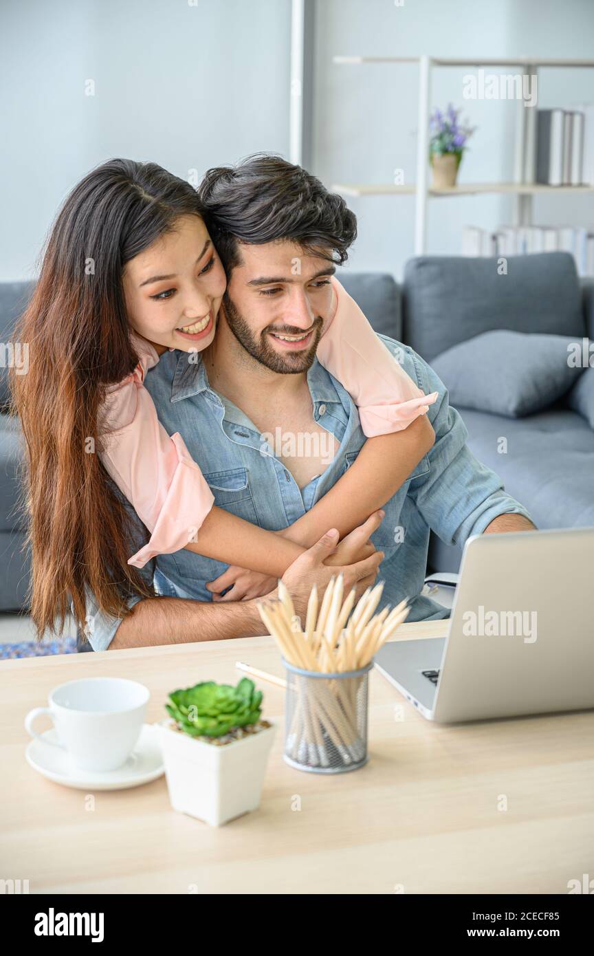 Happy and relax  lifestyle of young couple lover wearing casual dress together working on laptop notebook computer in living room at home. Positive re Stock Photo