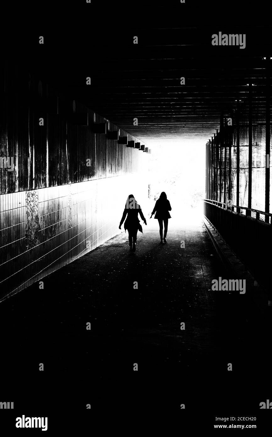Creative rough black and white image with grains of two young women in an urban tunnel rushing towards the light. Stock Photo