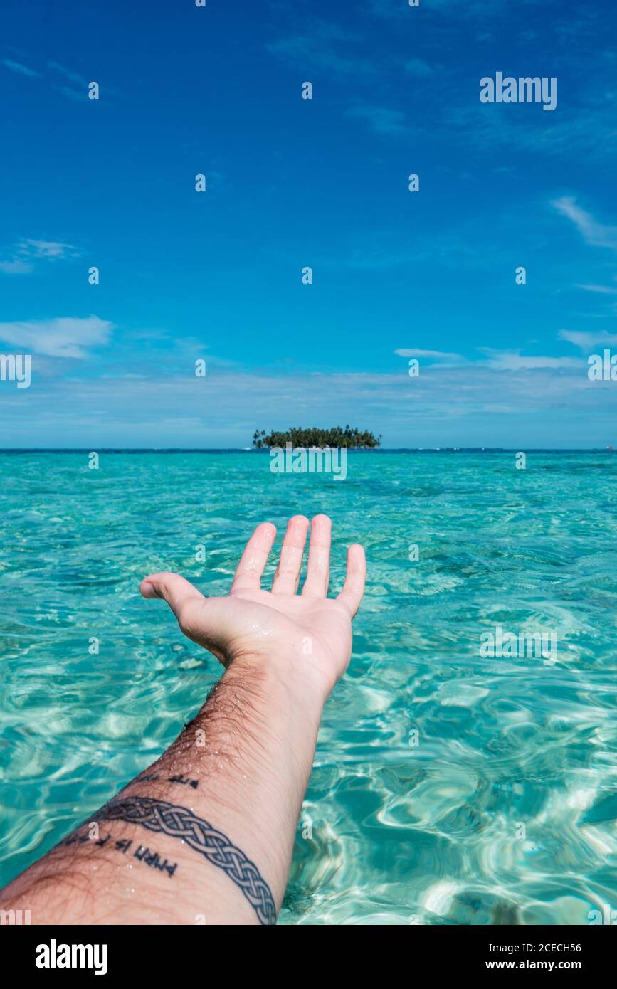 Crop male hand reached out to tropical trees between sea and blue sky in San Blas islands, Panama Stock Photo