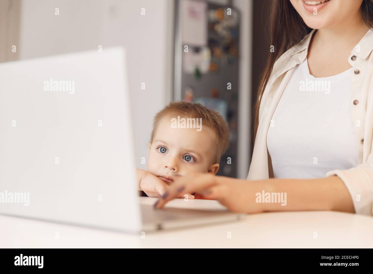 Business mom is using online work laptop, woman spending time with her boy baby home Stock Photo