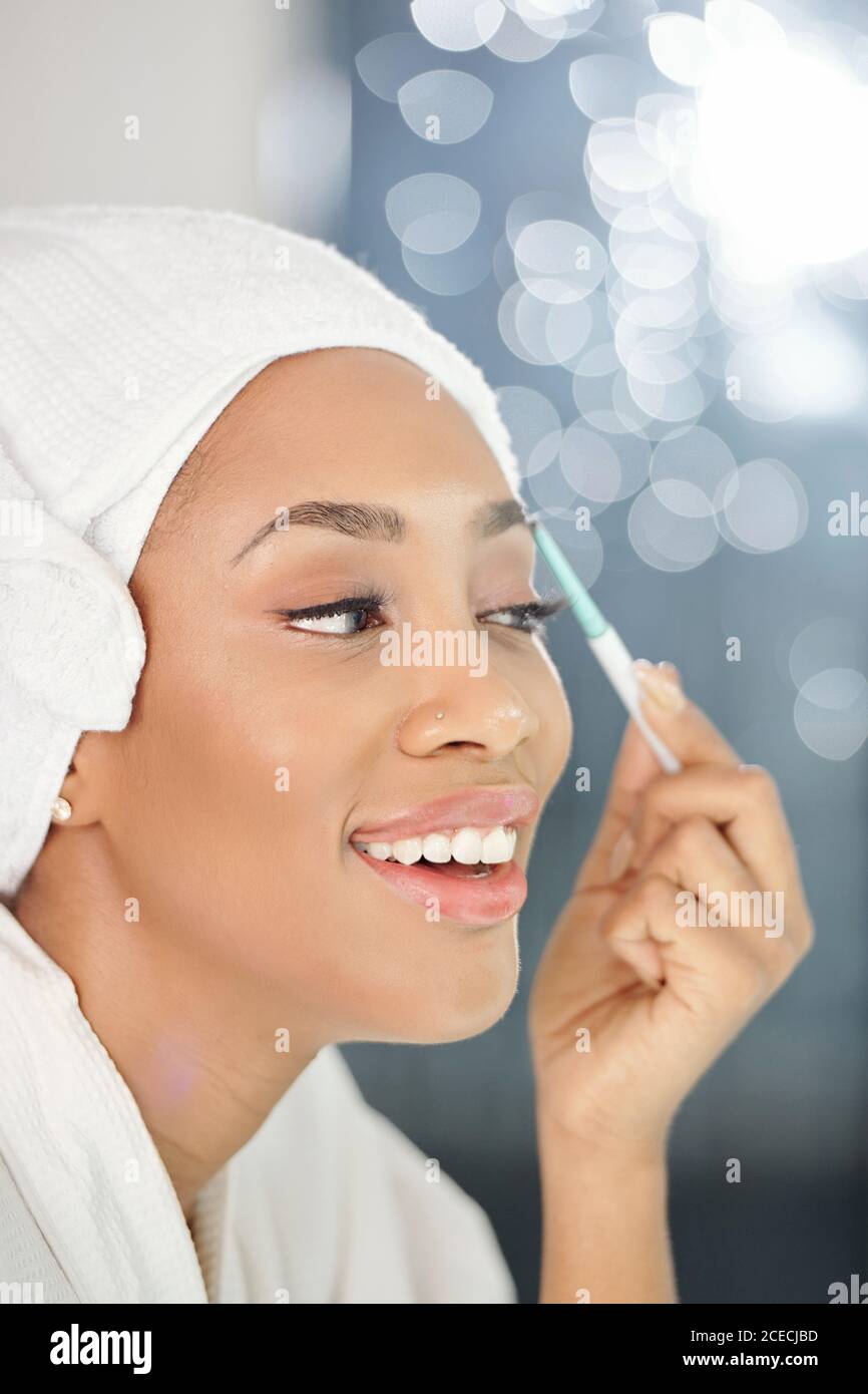 Happy beautiful young Black woman trimming eyesbrows with electric