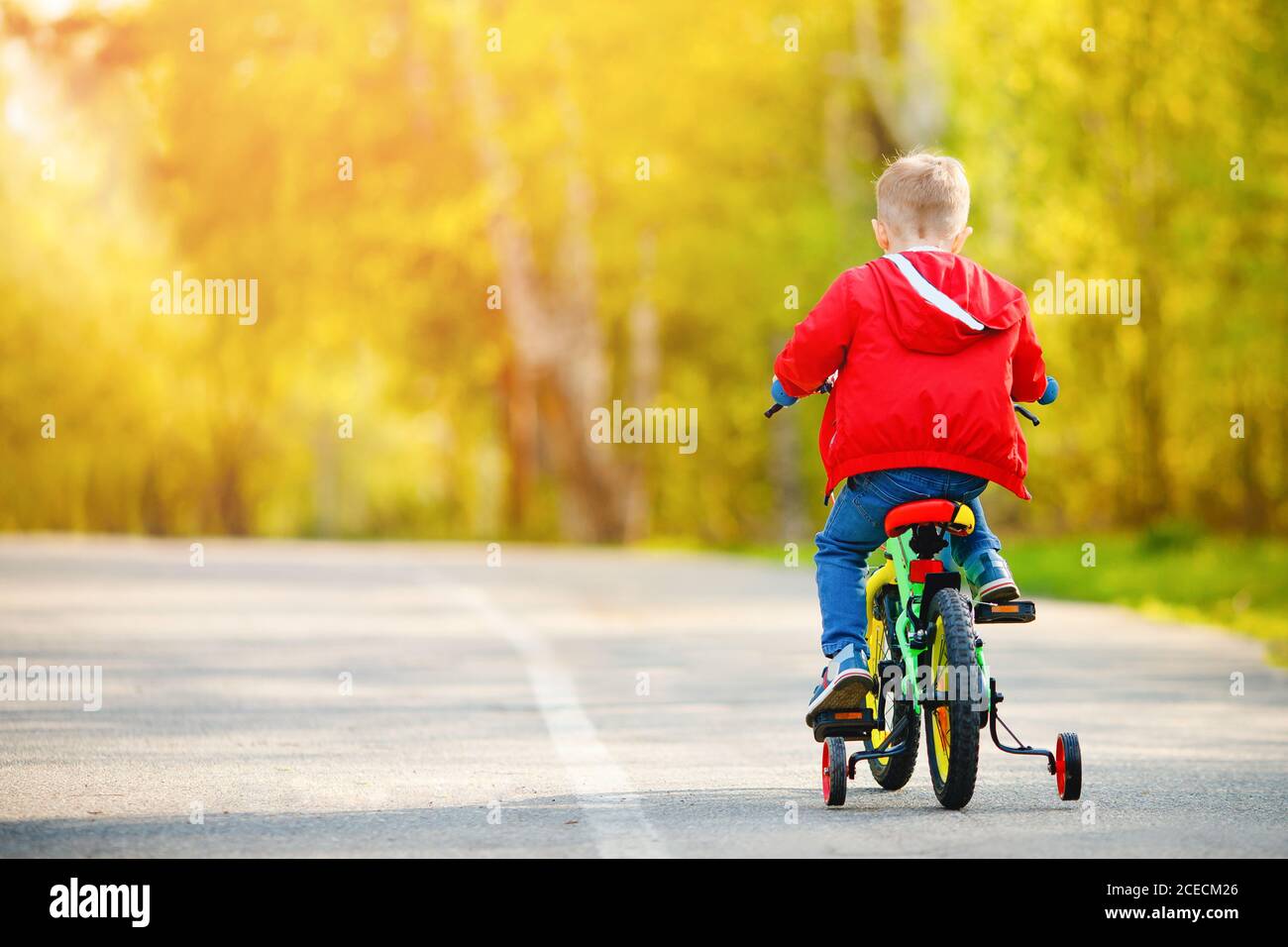 Boy kid training to ride bicycle with supporting wheels on sides, back