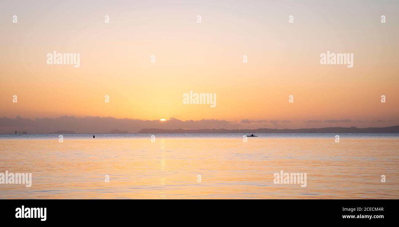 Sun rising over the clouds, a tiny boat paddling in the pastel coloured ocean Stock Photo
