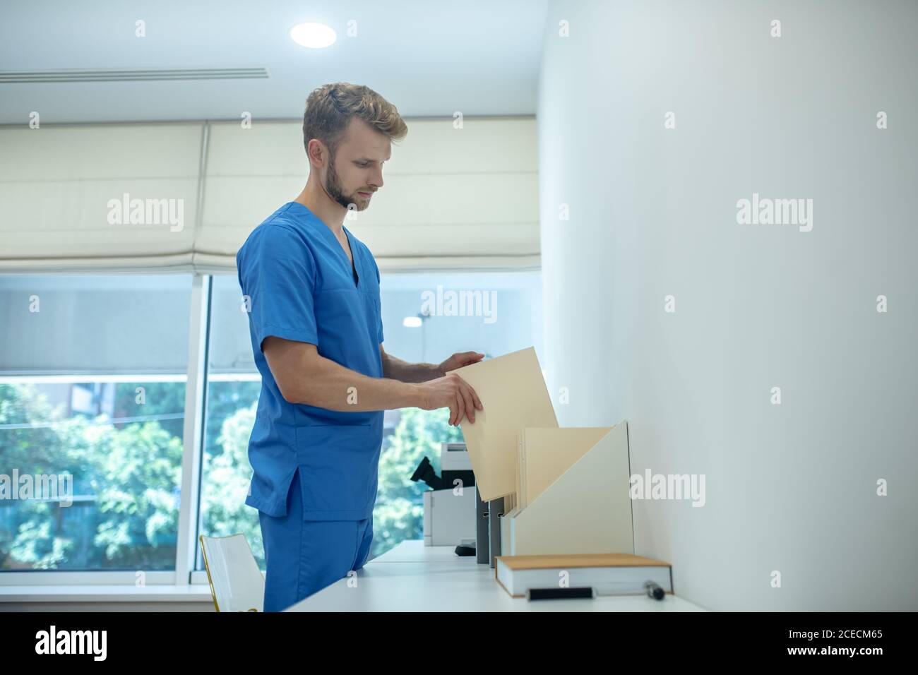 Bearded young doctor putting envelope in standing file folder Stock ...