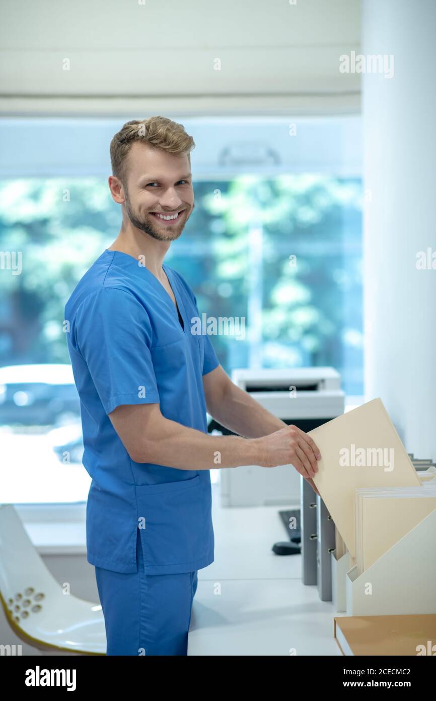 Bearded young doctor in putting envelope in standing file folder ...