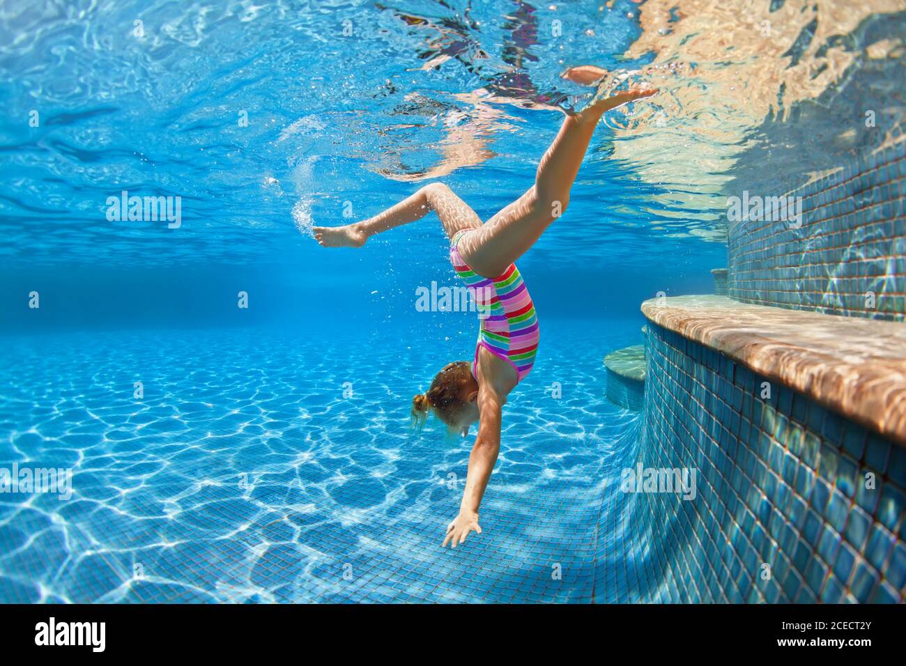 Funny child learning swimming, dive in blue pool with fun - jumping deep down underwater with splashes. Healthy family lifestyle, kids activity Stock Photo