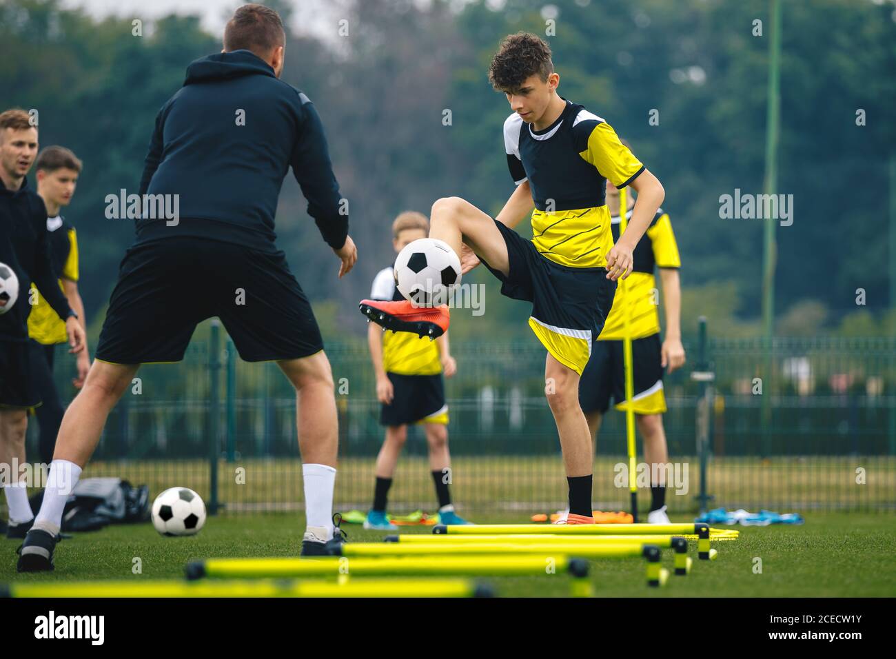 Teenagers on soccer training camp. Boys practice football witch young coaches. Junior level athletes improving soccer skills on outdoor training. Play Stock Photo