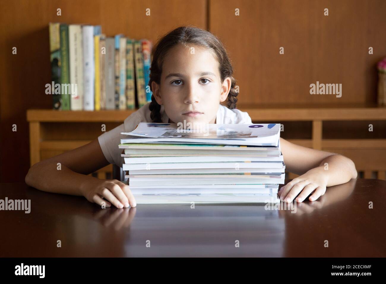 Young student tired of studying looking towards the camera next to a pile of books Stock Photo
