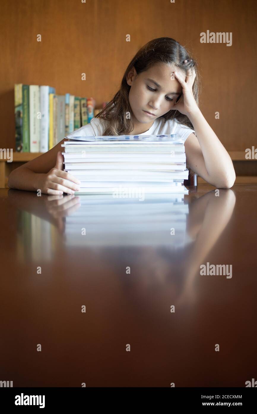 Girl exhausted from studying next to a pile of books looking down Stock Photo