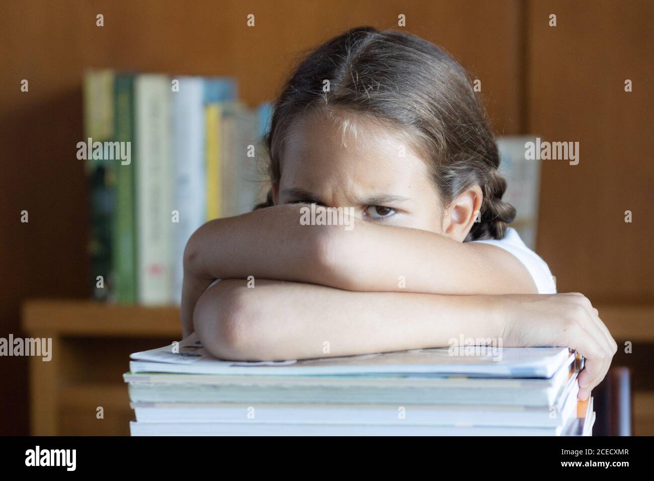 Angry student girl leaning against a pile of textbooks with a frown Stock Photo