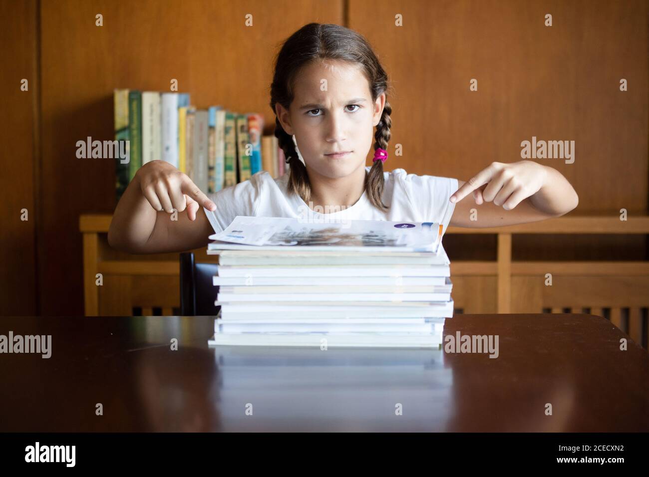 Angry student girl pointing to a pile of textbooks alone at home Stock Photo
