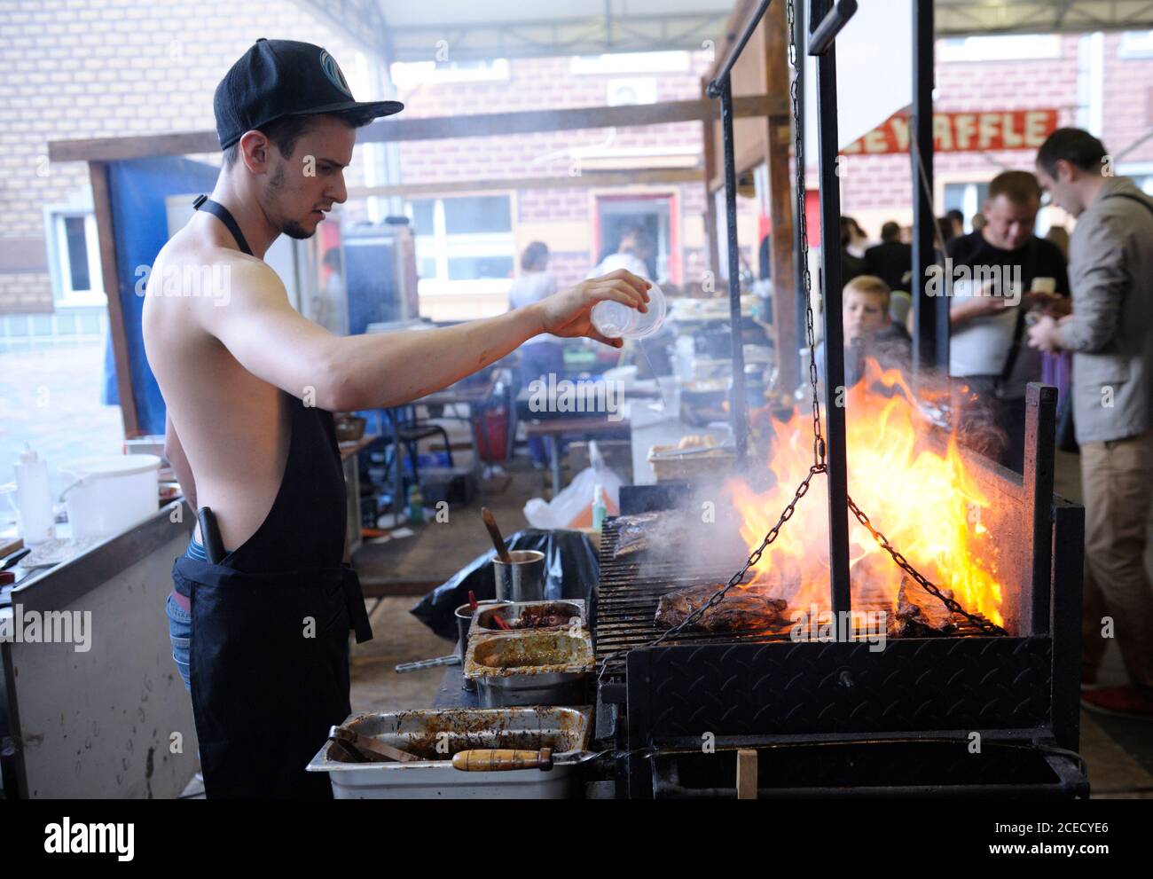 Cook watering barbecue from a bottle trying to extinguish flame, people ...