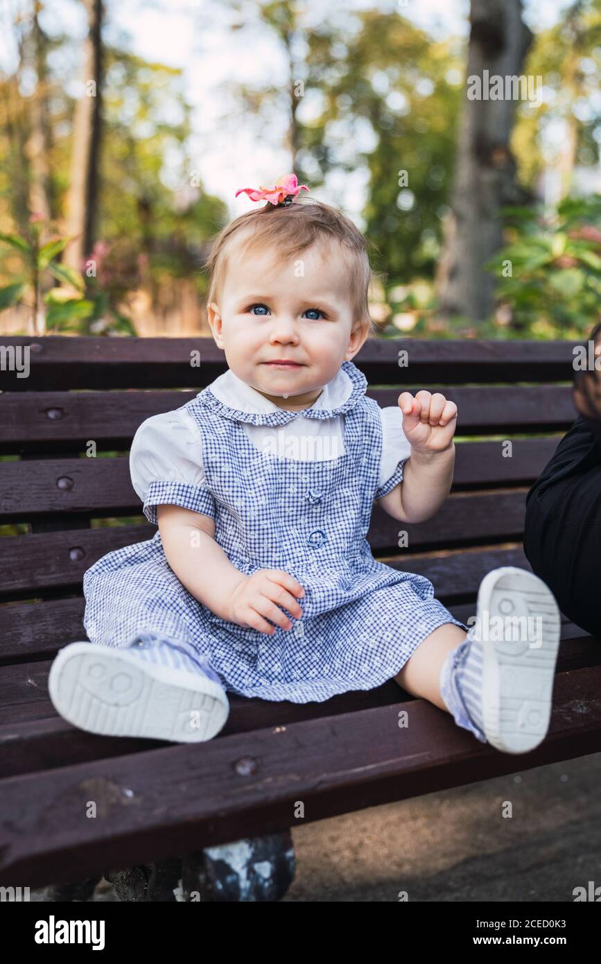 Cute baby girl in checkered dress looking at camera while sitting on