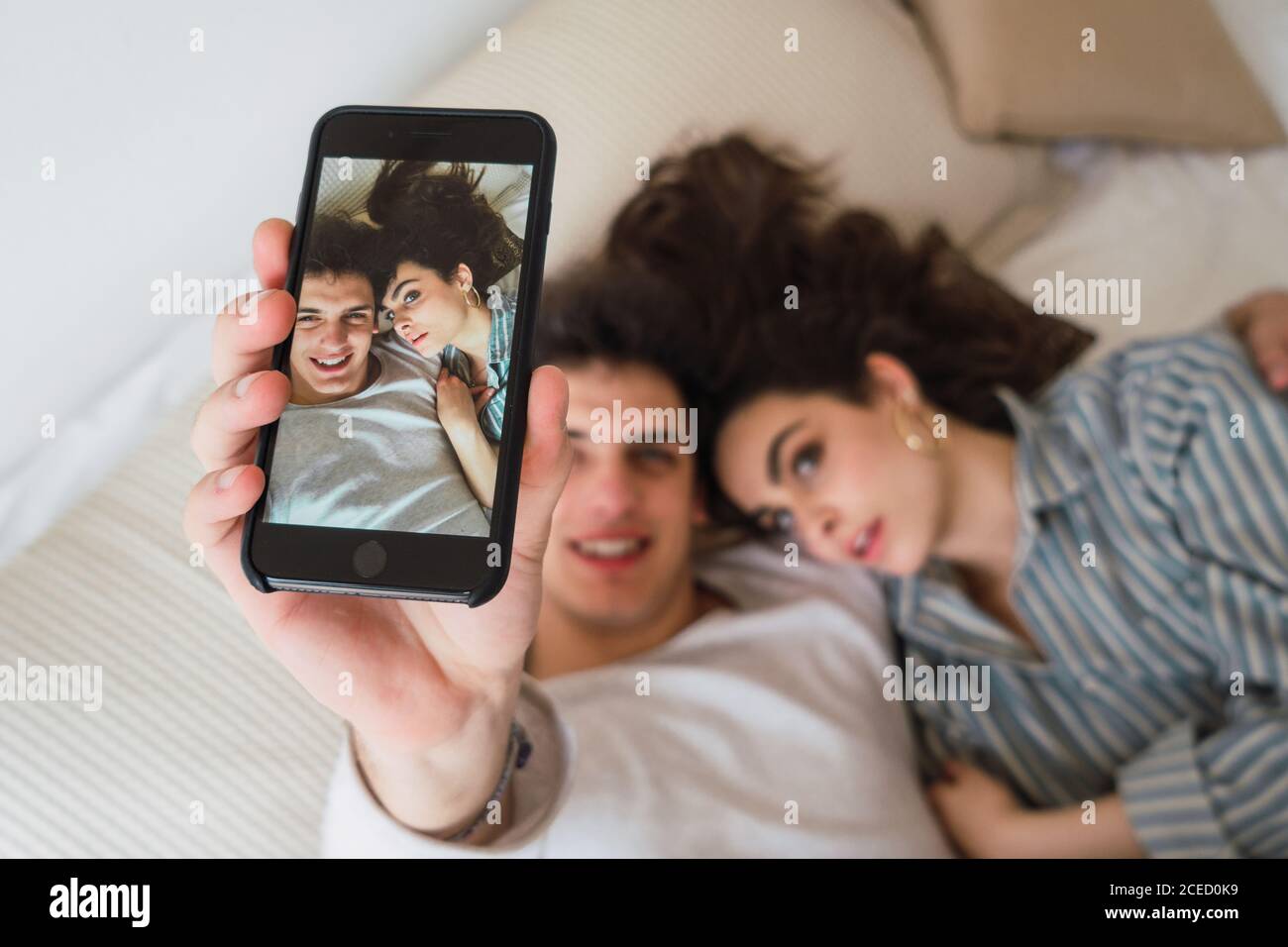 From above cheerful young man and Woman lying on bed and taking selfie with smartphone. Stock Photo
