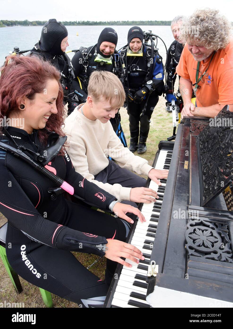 31 August 2020, Saxony, Leipzig: On the beach of the Kulkwitzer See in front of the diving school Delphin, the 15-year-old pianist Florian shows his group of sport divers from Ulm/Neu-Ulm (Baden-Württemberg/Bavaria) and diver Selina Schwarz from Leipzig (front right) different keystrokes on an old grand piano from 1880 which is placed outside. During a festival lasting several days, the 4th Leipzig Keyboard Days (until 13.09.20), a total of ten pianos and grand pianos sponsored by institutions and companies will be on display at various locations in the large new building area. The musical ins Stock Photo
