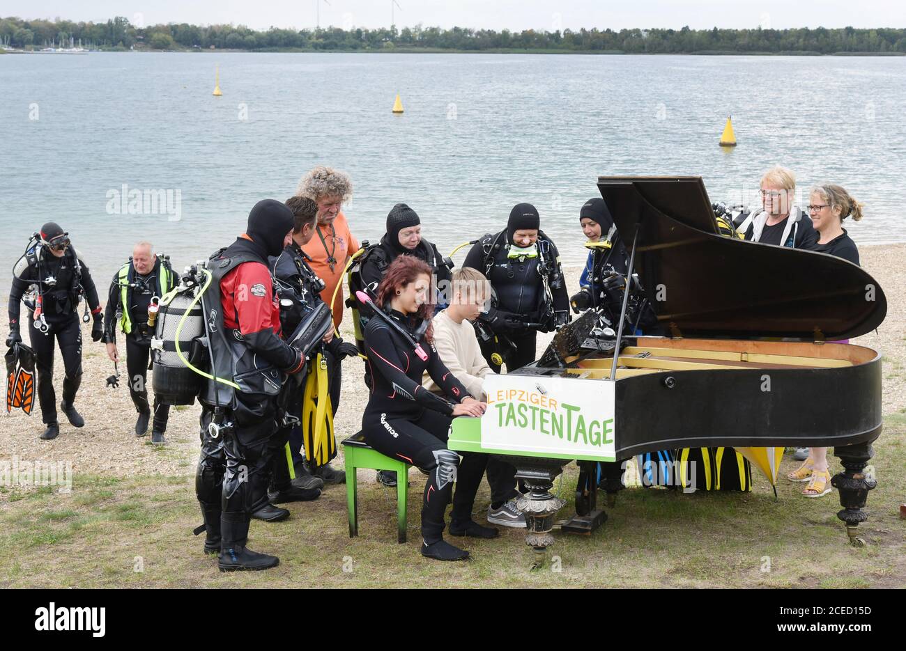 31 August 2020, Saxony, Leipzig: On the beach of the Kulkwitzer See in front of the diving school Delphin, the 15-year-old pianist Florian shows his group of sport divers from Ulm/Neu-Ulm (Baden-Württemberg/Bavaria) and diver Selina Schwarz from Leipzig (front right) different keystrokes on an old grand piano from 1880 which is placed outside. During a festival lasting several days, the 4th Leipzig Keyboard Days (until 13.09.20), a total of ten pianos and grand pianos sponsored by institutions and companies will be on display at various locations in the large new building area. The musical ins Stock Photo