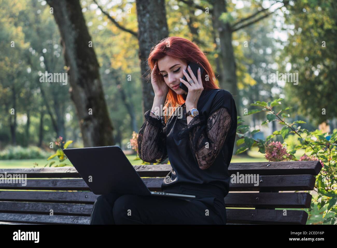 Woman using laptop and smartphone on bench Stock Photo
