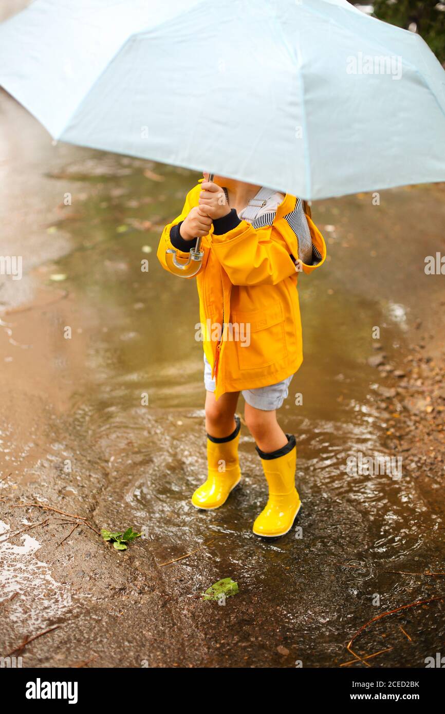 Little girl wearing yellow coat and boots under blue umbrella in rainy