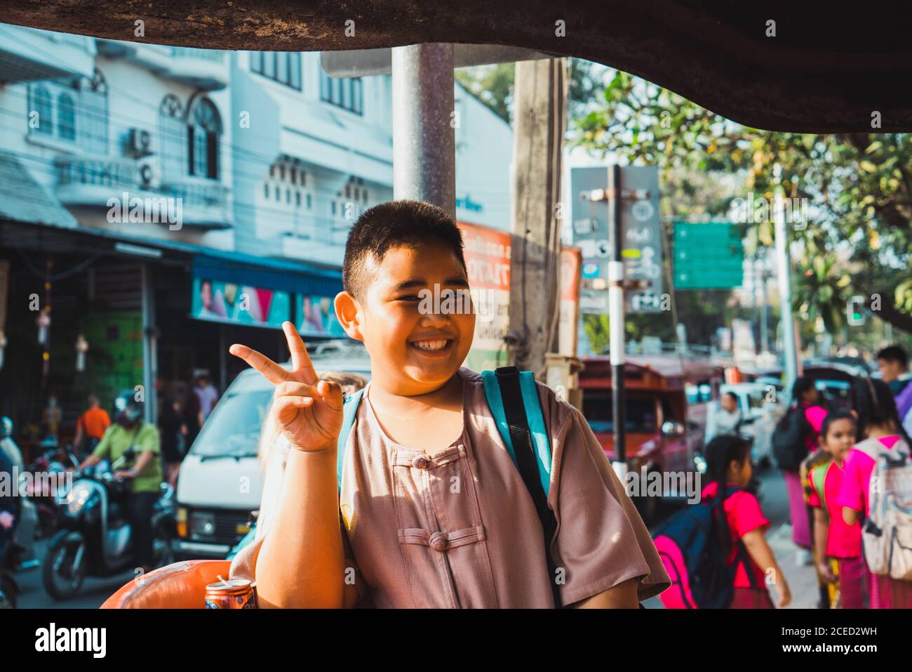 Cheerful chubby Asian boy gesturing two fingers on town street. Stock Photo