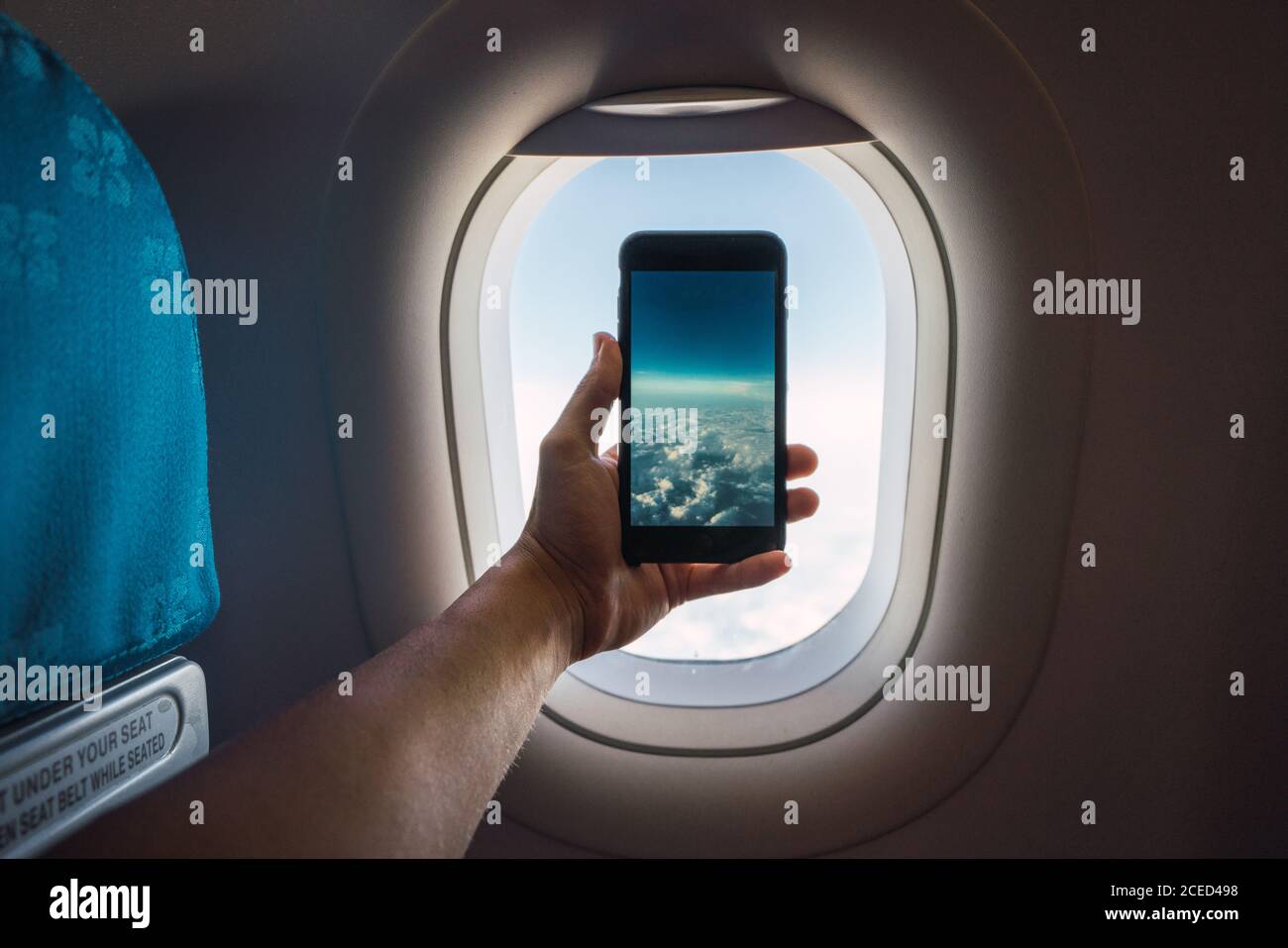 Crop hand holding smartphone and taking picture of infinite white clouds behind window of plane Stock Photo