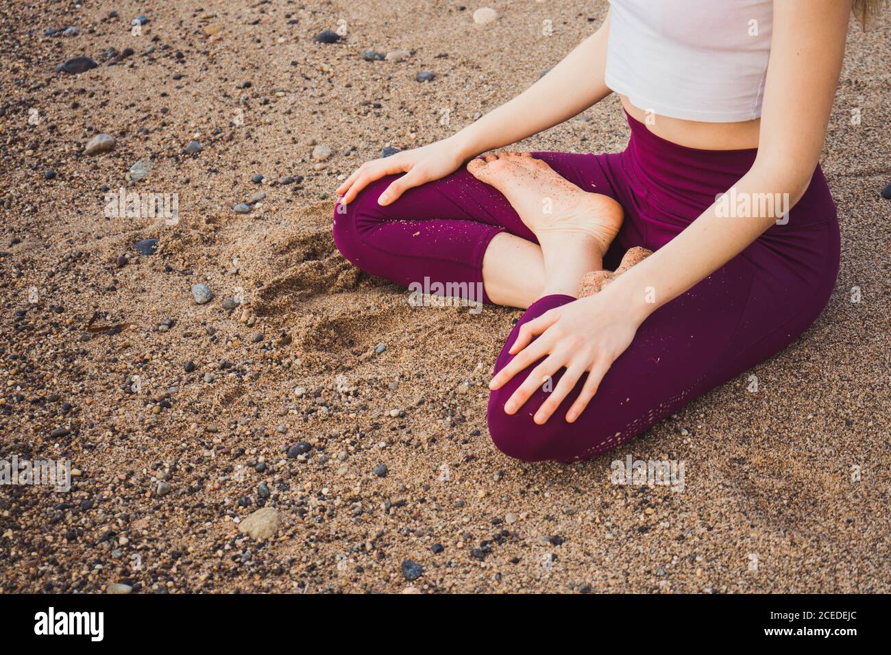 Crop unrecognizable Woman sitting on wet sand and meditating. Stock Photo