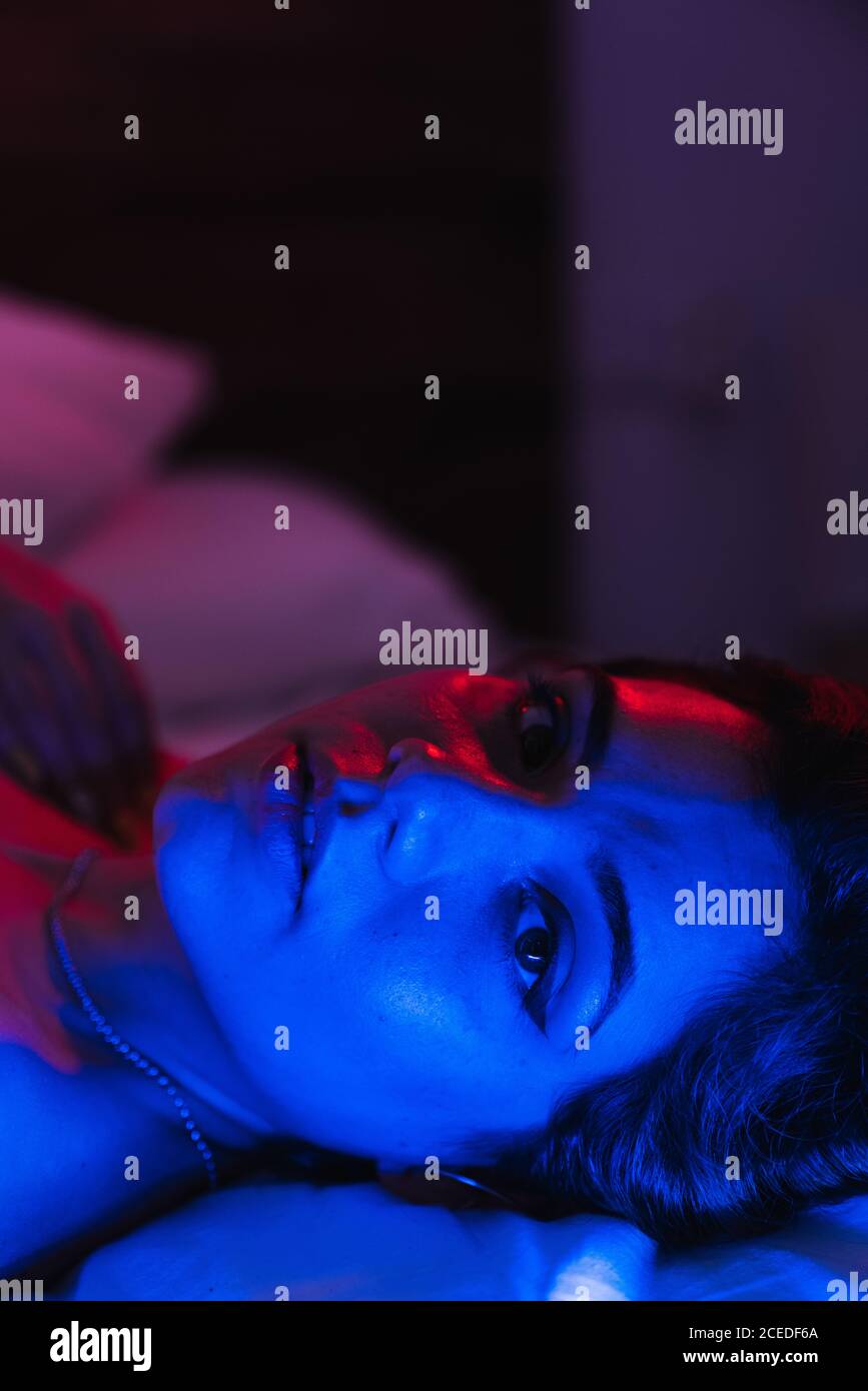 Lovely young female looking at camera while lying on nice bed in room