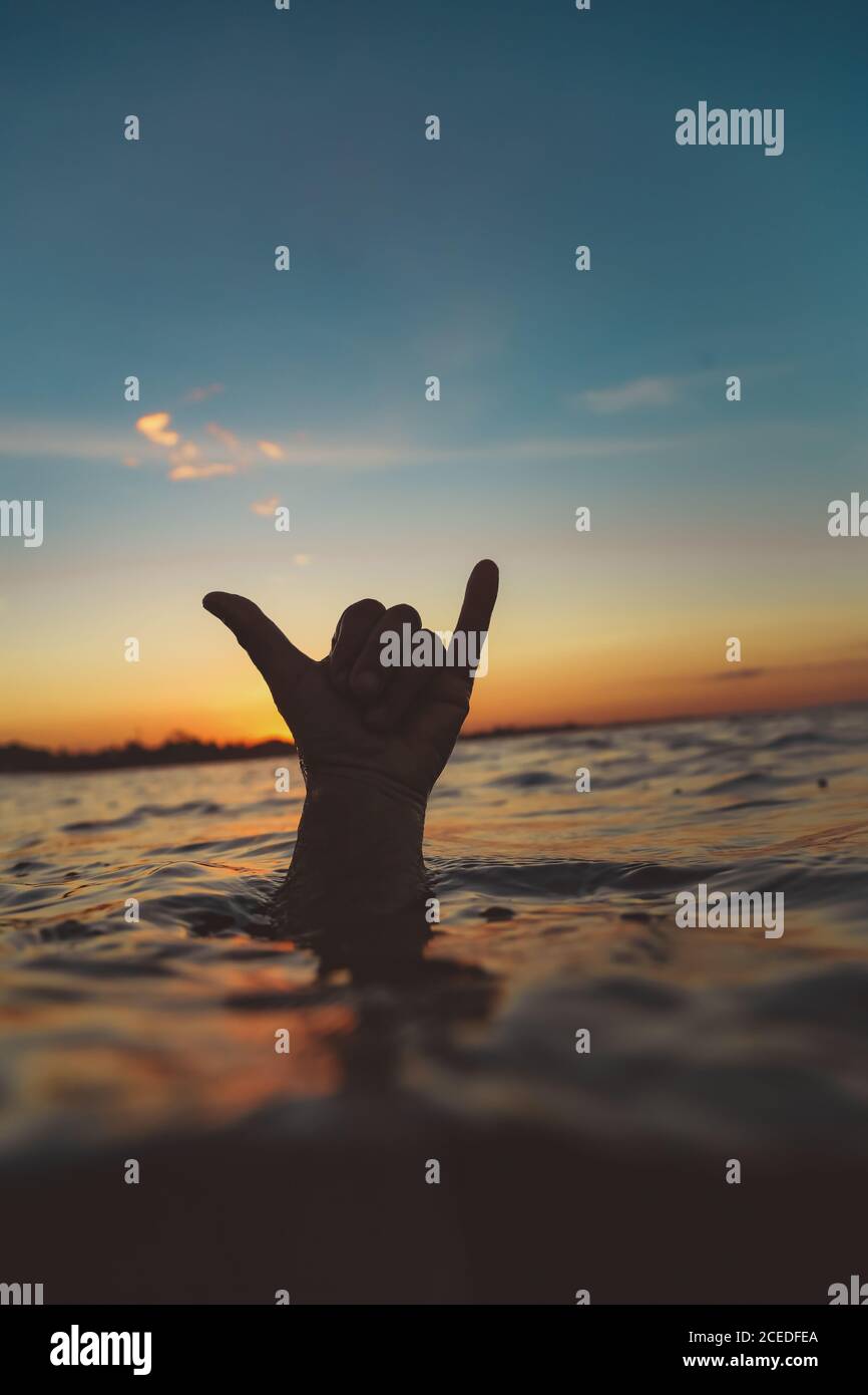 Closeup hand of human showing shaka sign above water surface with ripple and blue heaven in evening on Bali, Indonesia Stock Photo