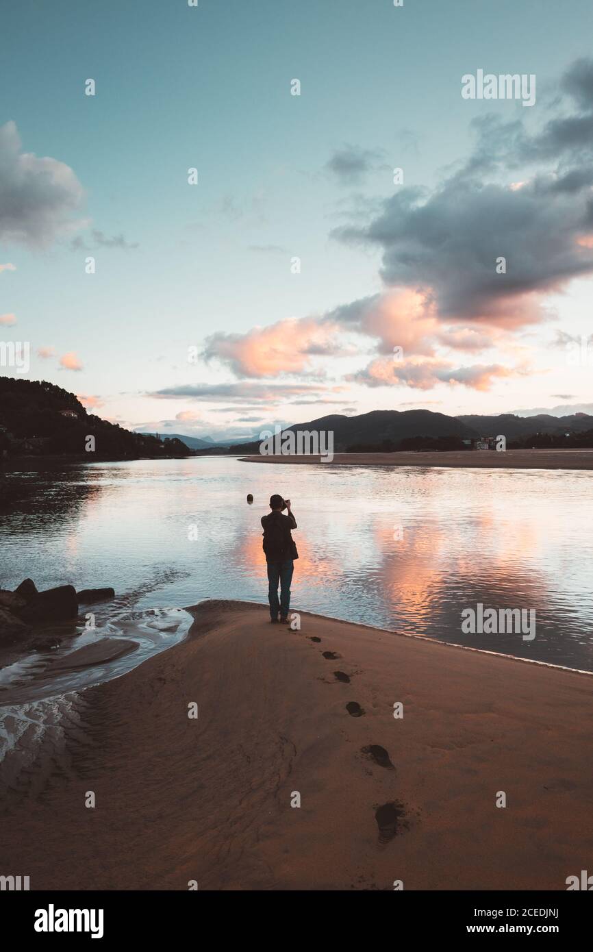 Back view of photographer on sandy beach of Laida with colorful sky reflecting in water, Bizkaia Stock Photo