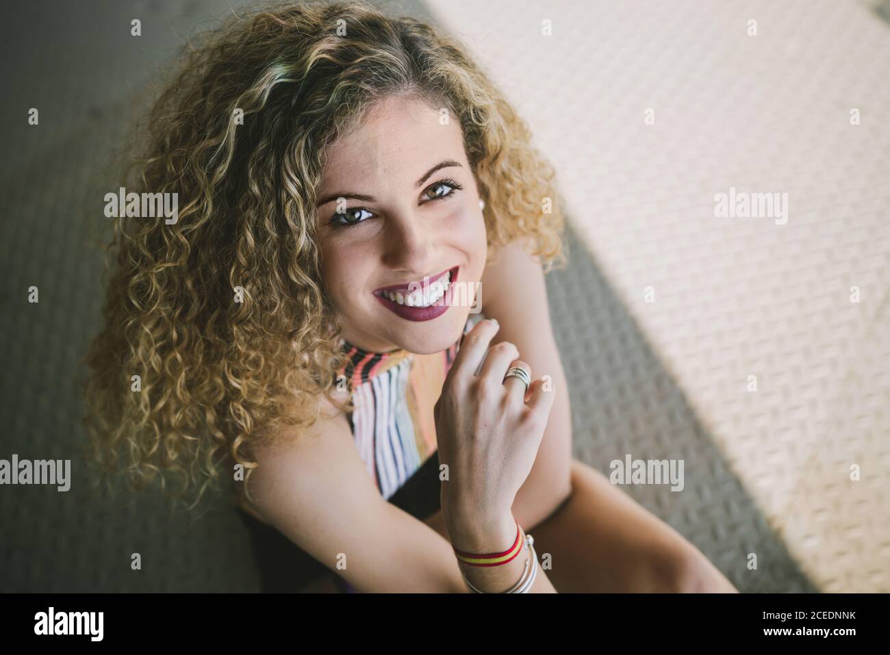 Portrait of beautiful young curly Woman with bright lips smiling cheerfully at camera sitting outdoors Stock Photo