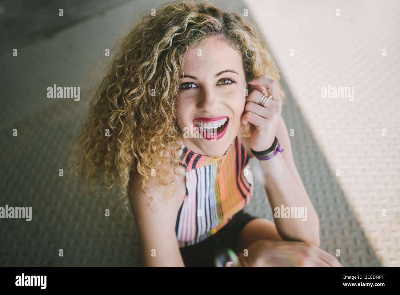 Portrait of beautiful young curly Woman with bright lips smiling cheerfully at camera sitting outdoors Stock Photo