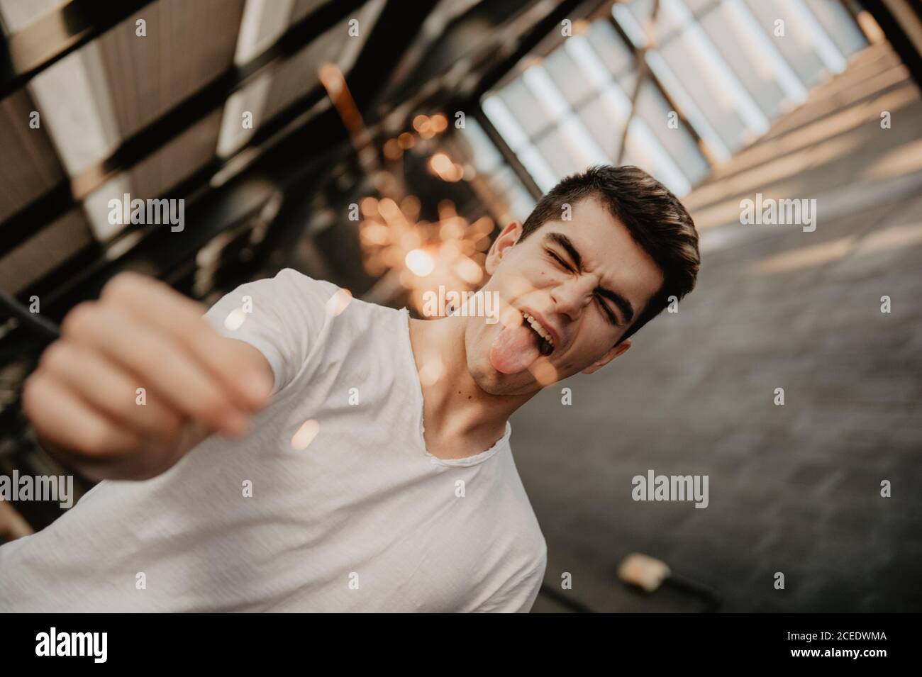 Young handsome man in white T-shirt standing inside building and holding burning Bengal light in hand Stock Photo