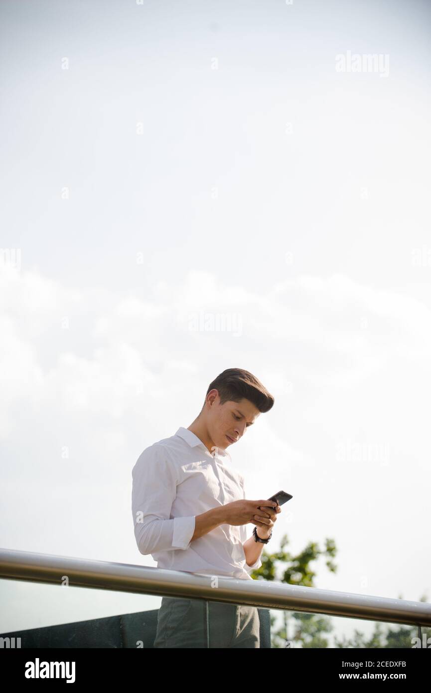 Young man with smartphone leaning on railing Stock Photo