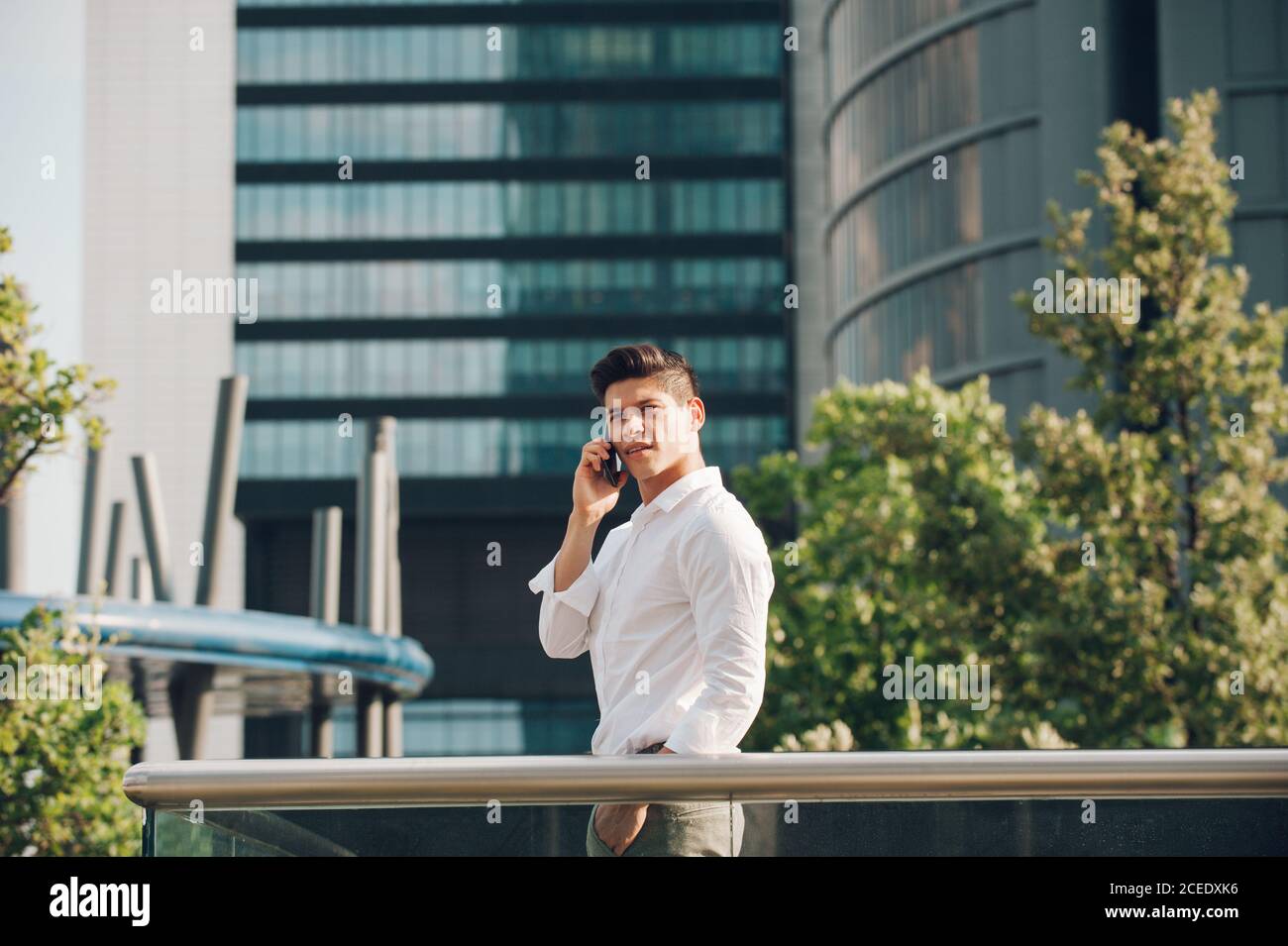 Young man with smartphone leaning on railing Stock Photo