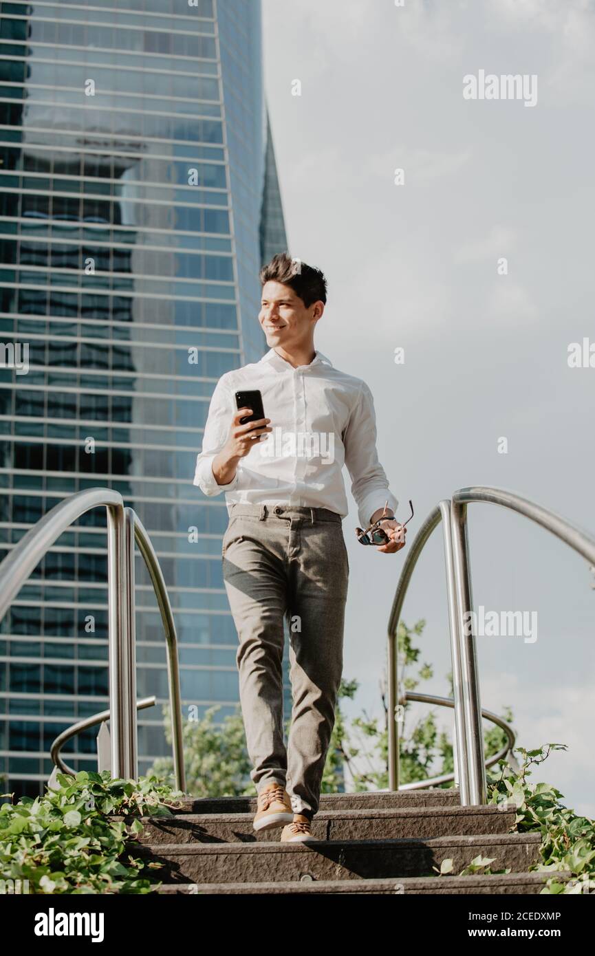 Cheerful man with smartphone walking down steps Stock Photo