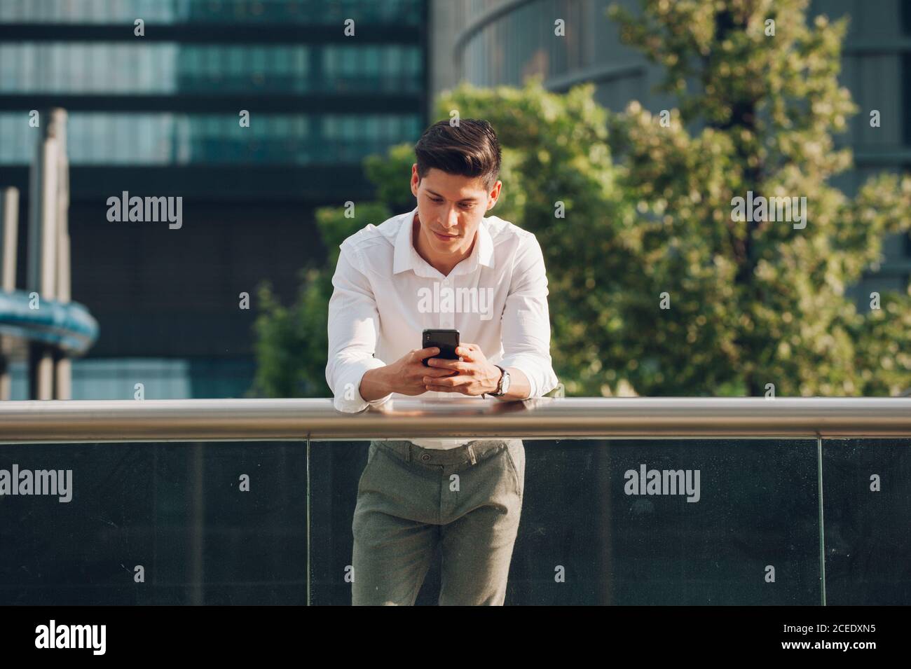 Young man with smartphone leaning on railing Stock Photo