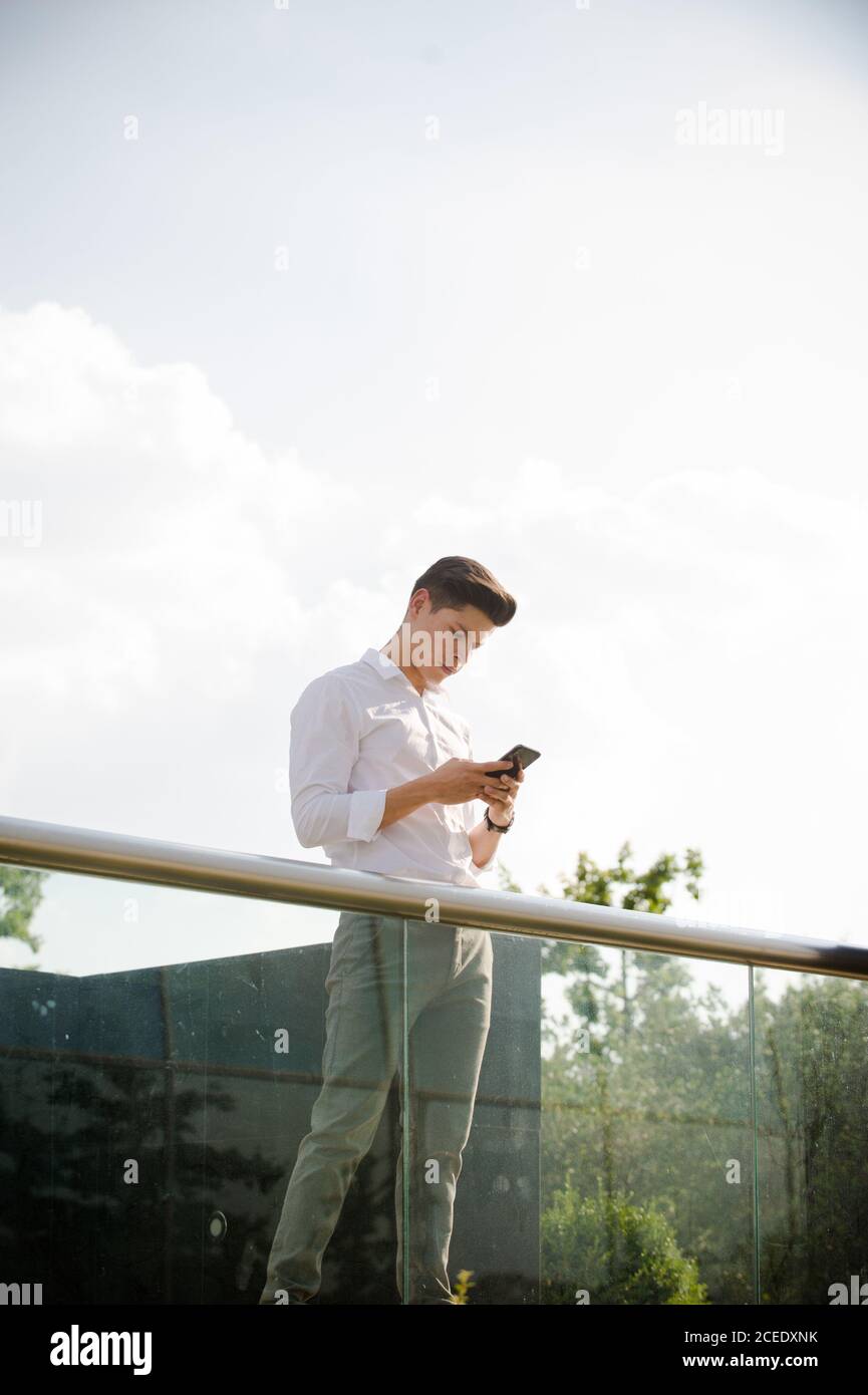 Young man with smartphone leaning on railing Stock Photo