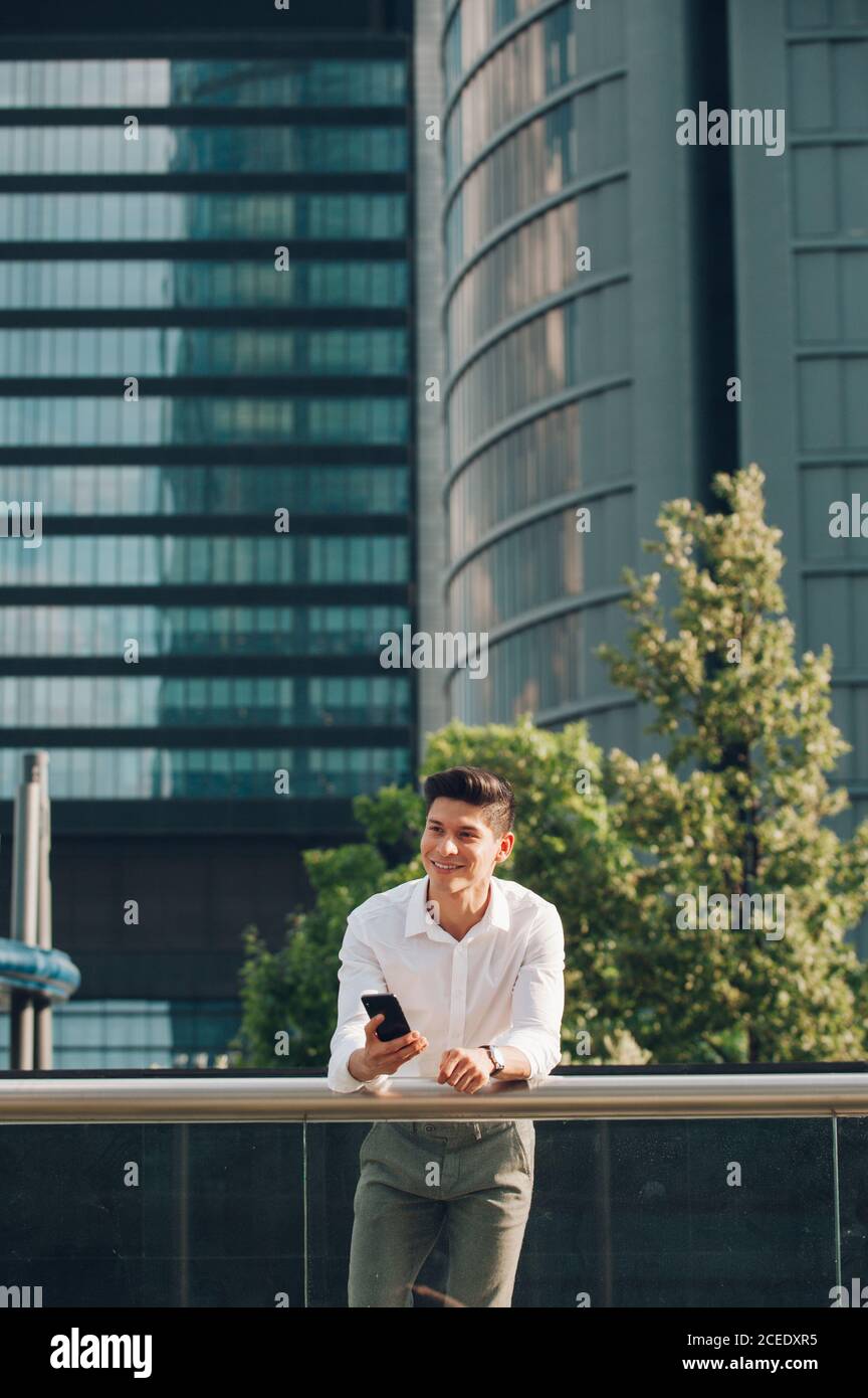 Young man with smartphone leaning on railing Stock Photo