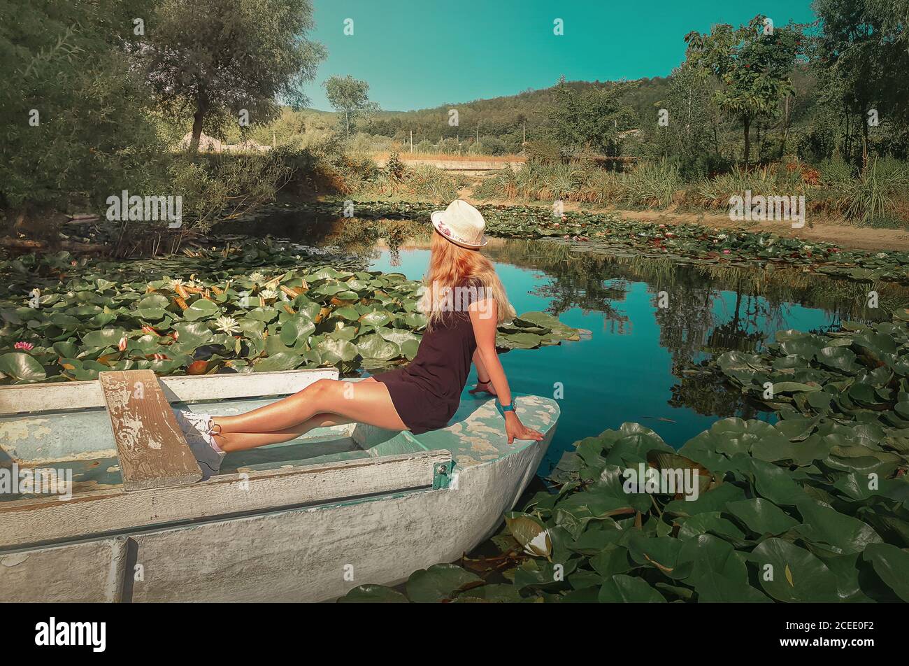 Carefree young woman floating relaxed on a boat at a pond with blooming waterlily, lotus flowers. Vacation travel, natural background at the lake with Stock Photo