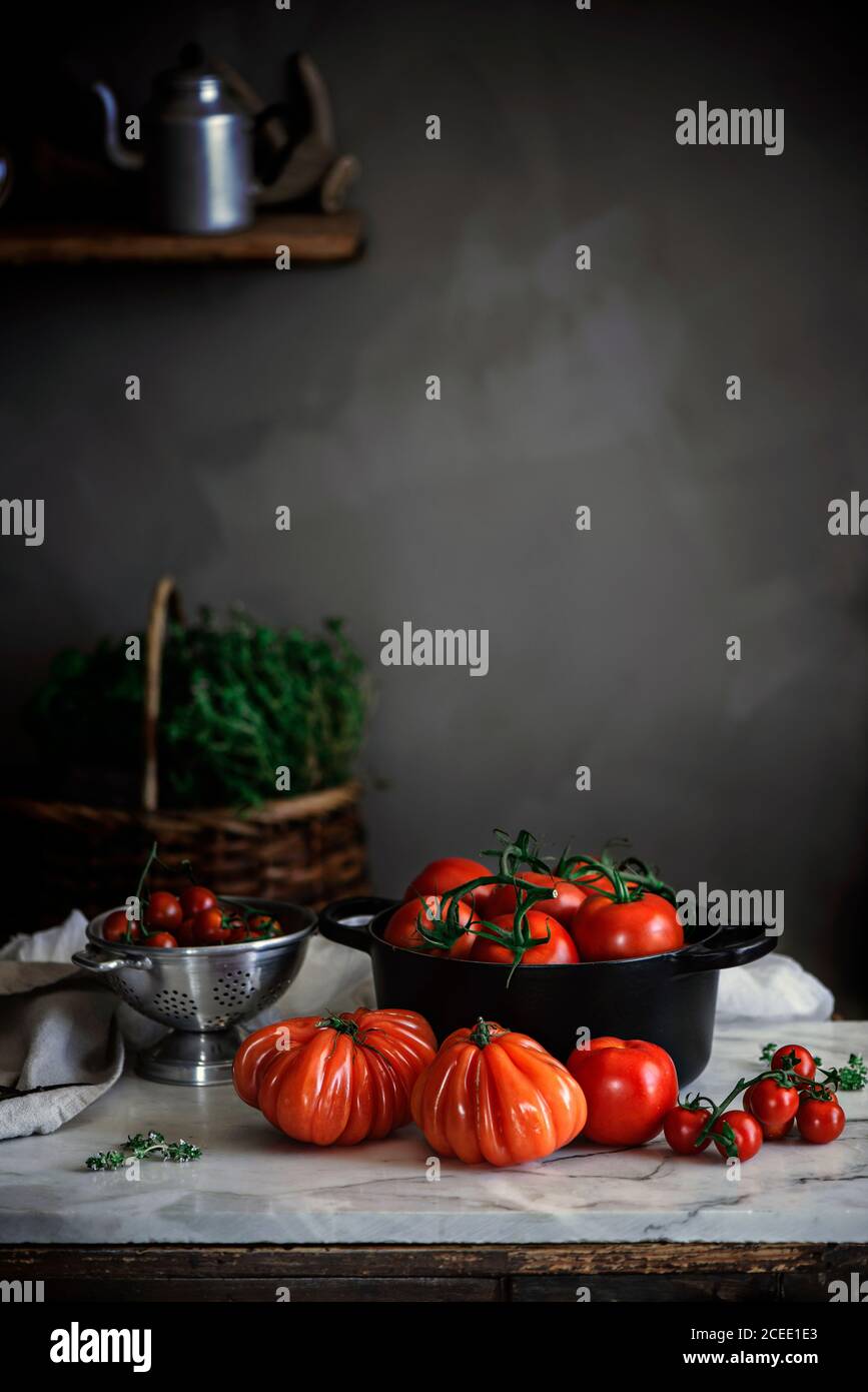 Big red ripe tomatoes of different forms in pot on table near grey wall Stock Photo
