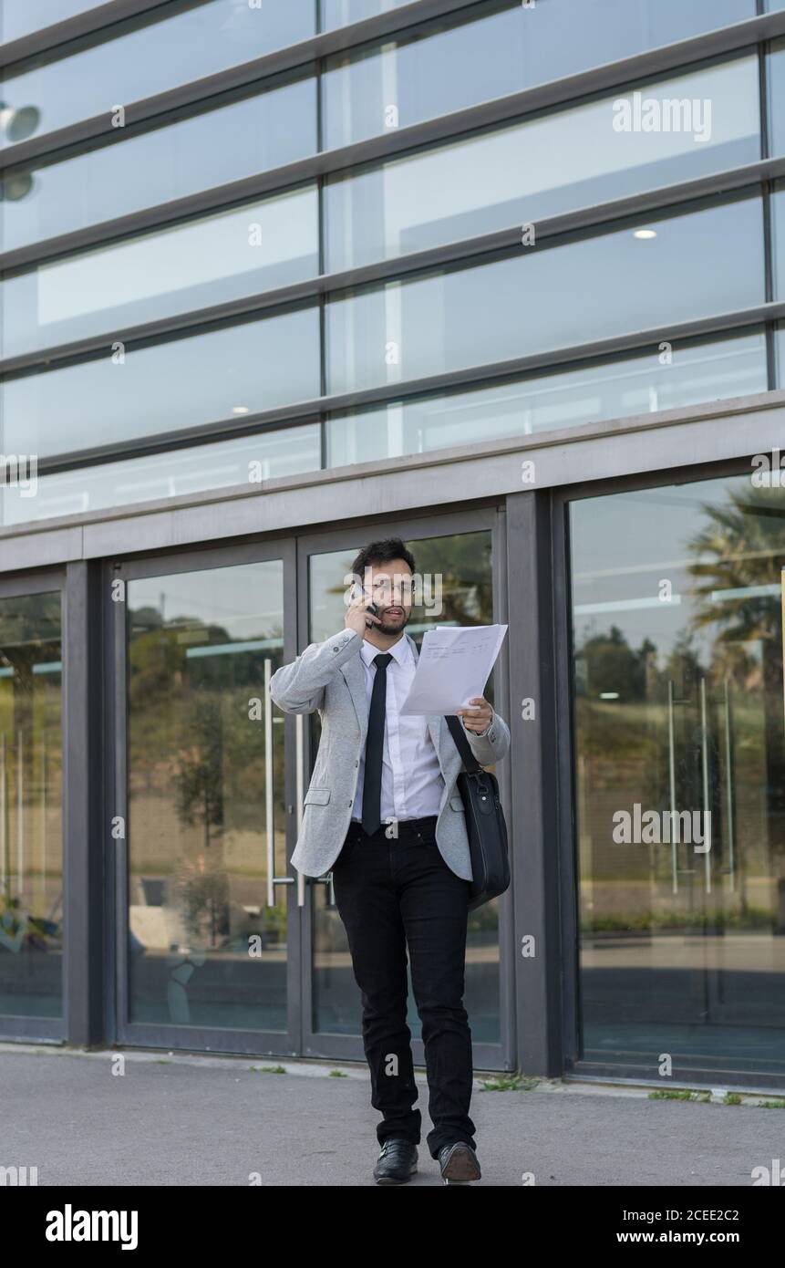 Latin businessman, leaving work from his office with his laptop and talking on the phone Stock Photo
