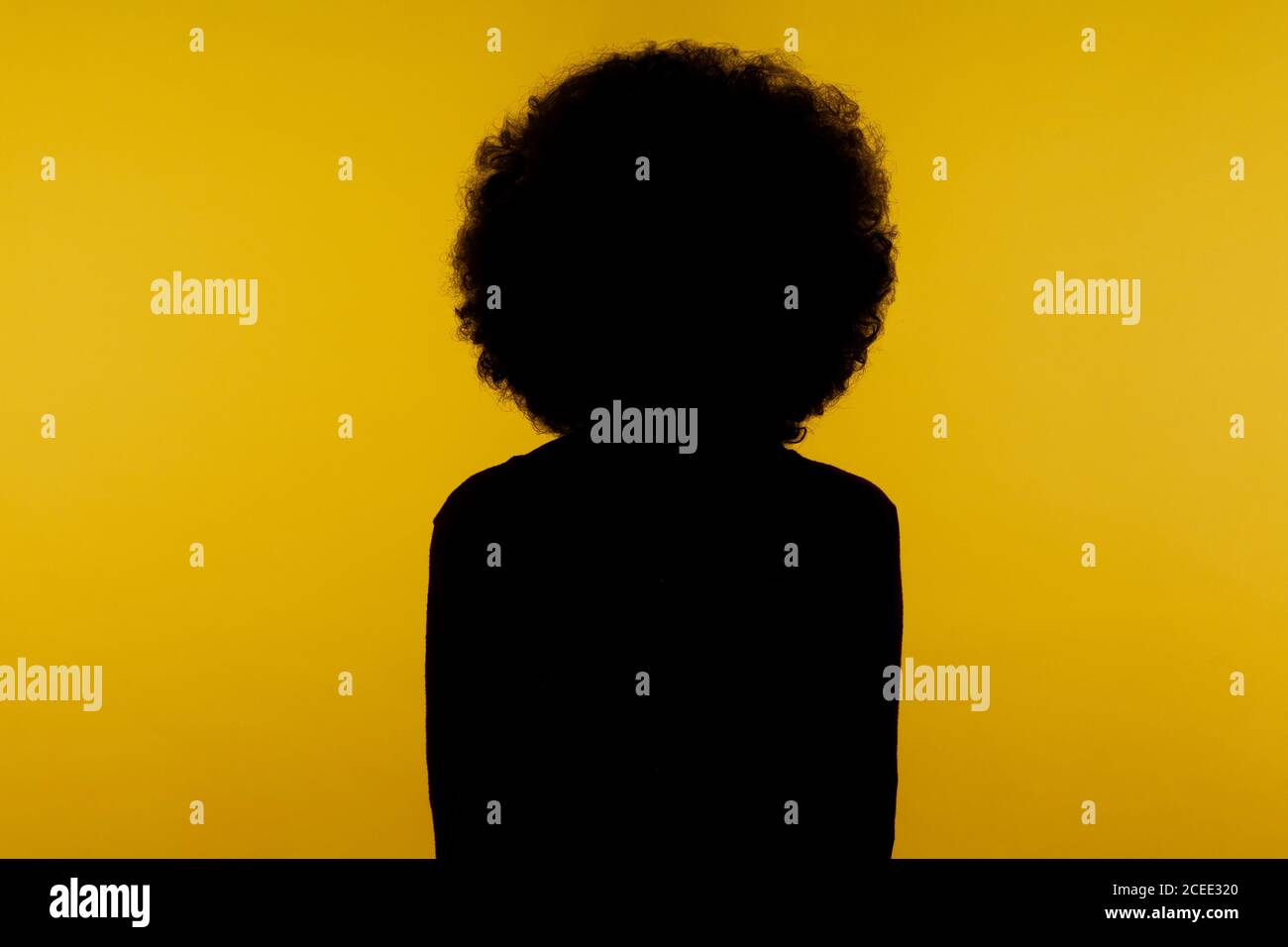 No name, anonymous hiding face in shadow, human identity. Silhouette portrait of curly hair person standing calm alone in darkness with hands down. in Stock Photo