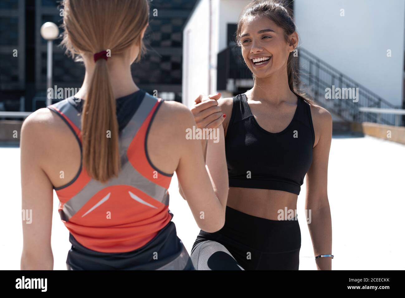 Two cheerful women in fitness wear giving high five while running in the city Stock Photo